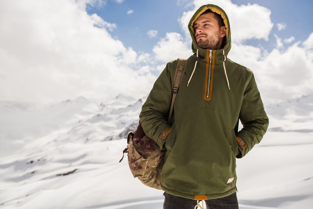 mladý muž v khaki bundě na túře v zasněžených horách