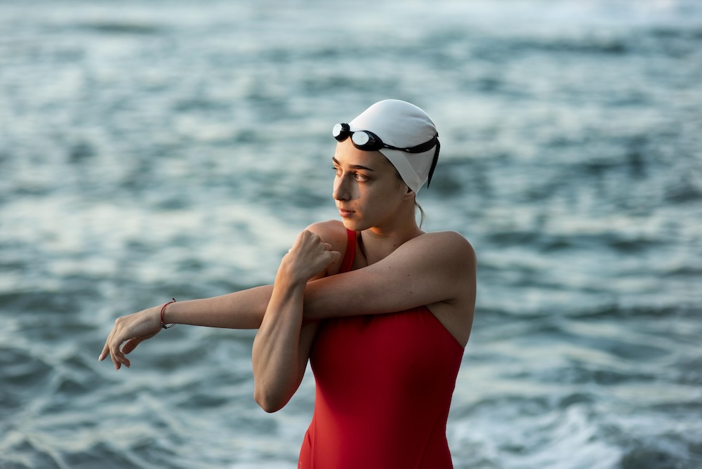 žena plavkyně v červených plavkách si protahuje ruce před plaváním