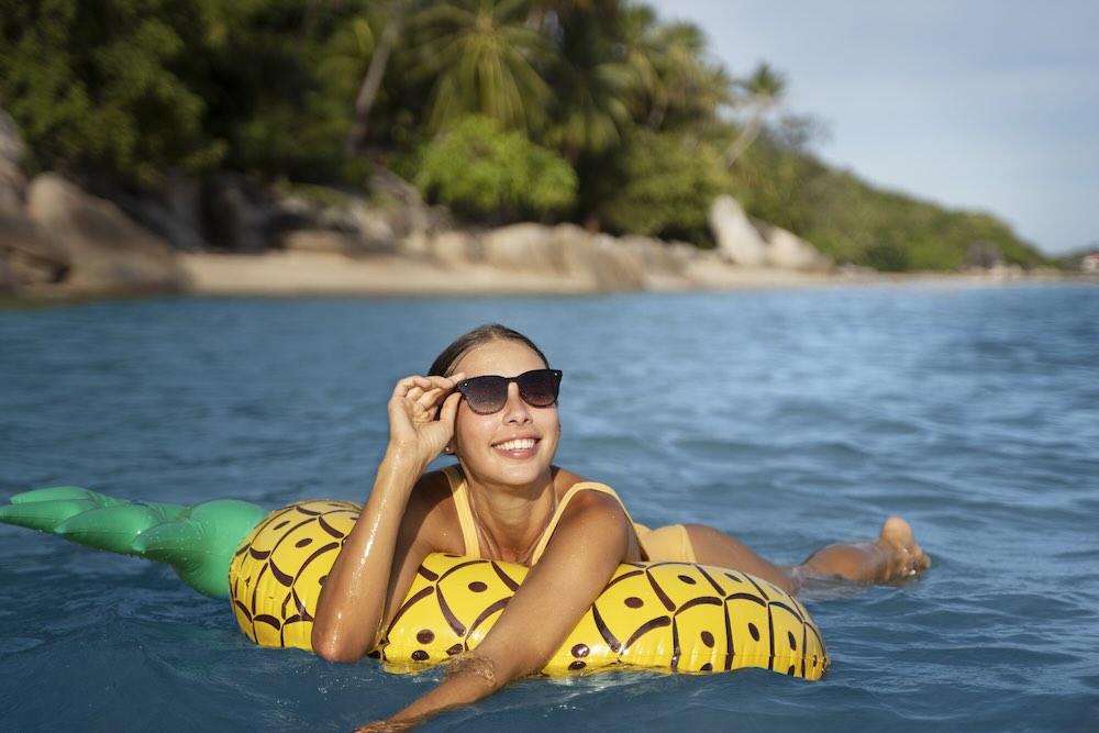žena ve slunečních brýlích plave na nafukovacím lehátku ve tvaru ananasu